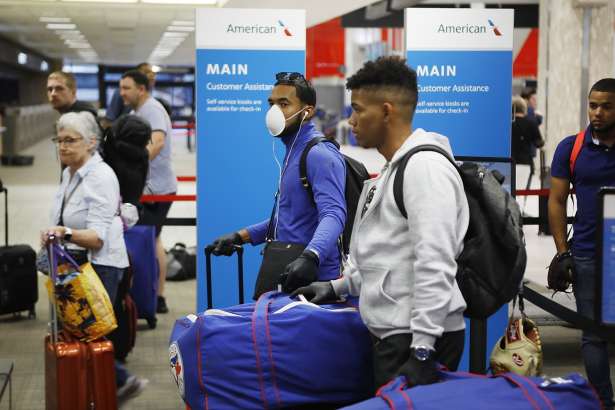 FILE - In this March 15, 2020, file photo, Toronto Blue Jays minor league baseball player Jesus Navarro, left center, wears a mask while he prepares to fly home along with his teammates from the Dominican Republic at Tampa International Airport in Tampa, Fla. Unlike the NFL, NBA or Major League Baseball that can run on television revenue, it's impossible for some minor sports leagues in North America to go on in empty stadiums and arenas in light of the coronavirus pandemic. These attendance-driven leagues might not play again at all in 2020, putting some teams in danger of surviving at all and potentially changing the landscape of minor league sports in the future. (Octavio Jones/Tampa Bay Times via AP, File)