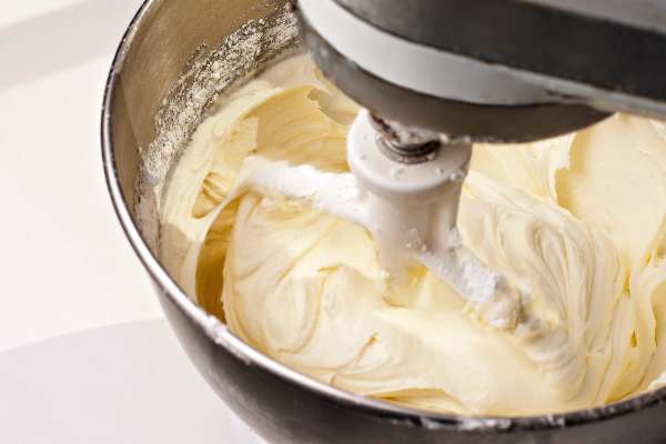 Electric mixer mixing yellow lemon cream cheese cake frosting. Shot during actual action and features some blur around beater.