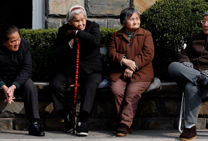 Elderly Chinese citizens sit together on a park bench.