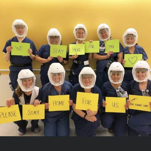 Nurses in PPE with signs reading: We stay here for you; please stay home for us