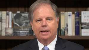 Doug Jones wearing a suit and tie smiling at the camera