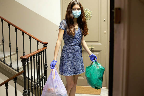 teenage girl in quarantine, wearing protective mask and gloves, in her hands she carries two garbage bags