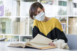 woman in a face covering reading in the library