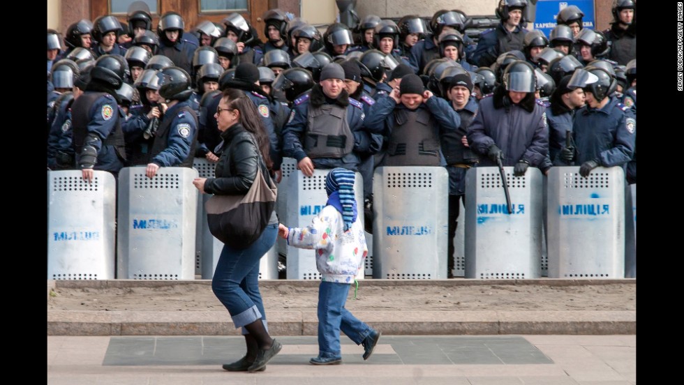 A woman and child walk past a line of police officers during a rally in Kharkiv on March 30.
