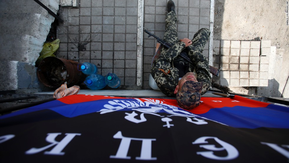An armed pro-Russian man sits below a flag of the self-proclaimed Donetsk People&#39;s Republic at the barricades on a road leading into Slovyansk on May 11. 