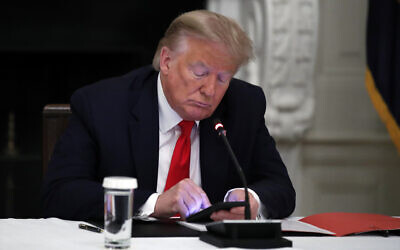US President Donald Trump looks at his phone during a roundtable with governors on the reopening of America's small businesses, in the State Dining Room of the White House, June 18, 2020, in Washington. (AP Photo/Alex Brandon)