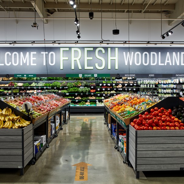 Produce section of a grocery store with the words "WELCOME TO FRESH WOODLAND HILLS" on the back wall.