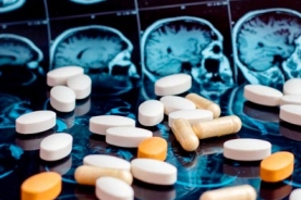 tablets and capsules of dementia prescription medications on a table with MRI images of a brain in the background