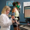 Researcher measuring breathing, heart rate, and blood pressure of participant while walking on a treadmill, results appear on a computer screen.
