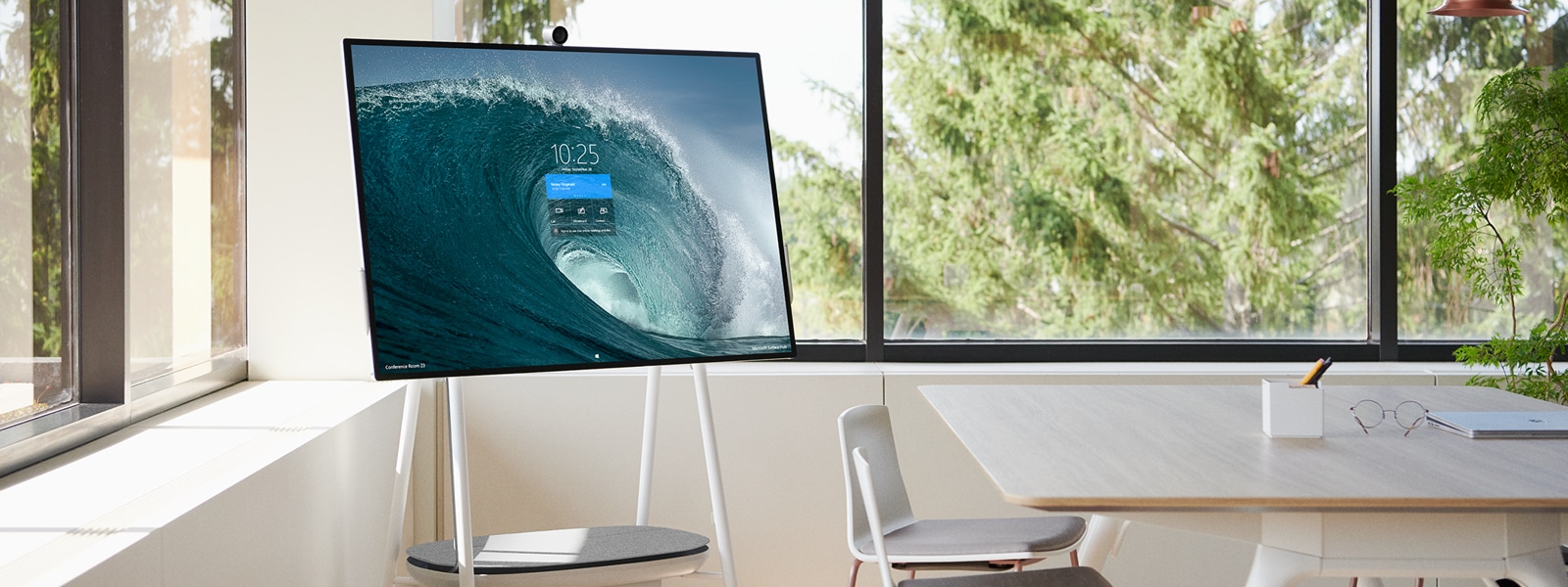 A Surface Hub 2 sits on a mobile stand and displays a start screen in a conference room.