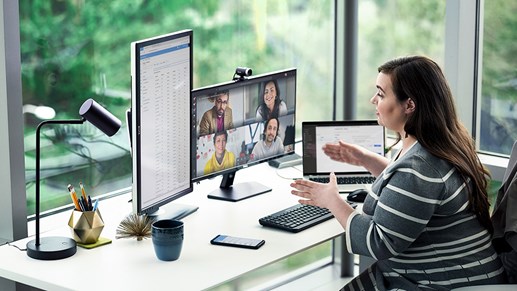 A person participating in a video call with 4 other individuals at their desk with multiple screens