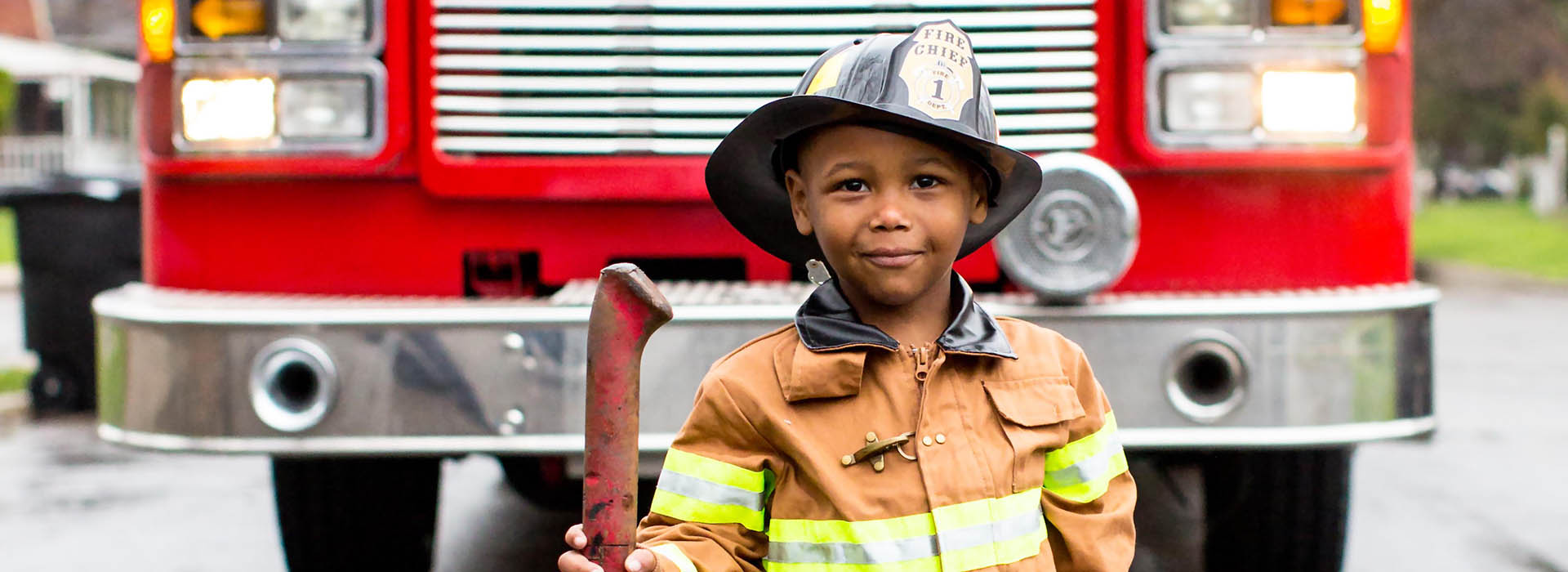 Child in a firefighter costume standing in front of a fire truck.