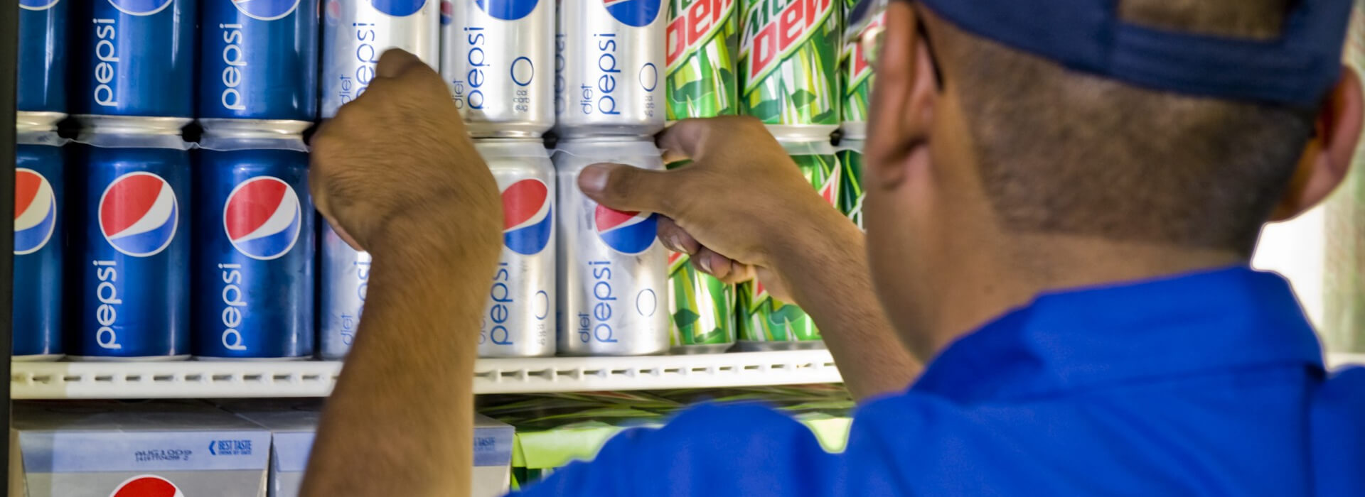 Worker loading cans of Pepsi into a refrigerator.