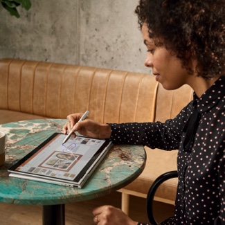 Woman sitting at a table using a stylus to write on a tablet 