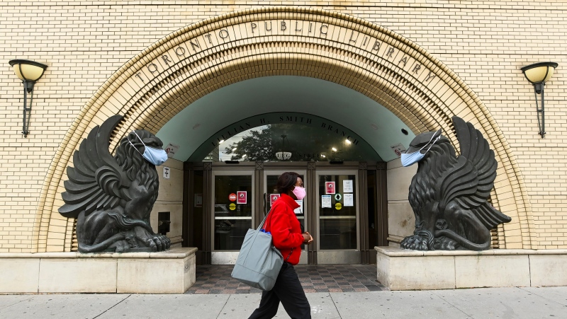 A woman walks past a Toronto Public Library where masks cover the faces of statues during the COVID-19 pandemic in Toronto on Friday, October 2, 2020. THE CANADIAN PRESS/Nathan Denette