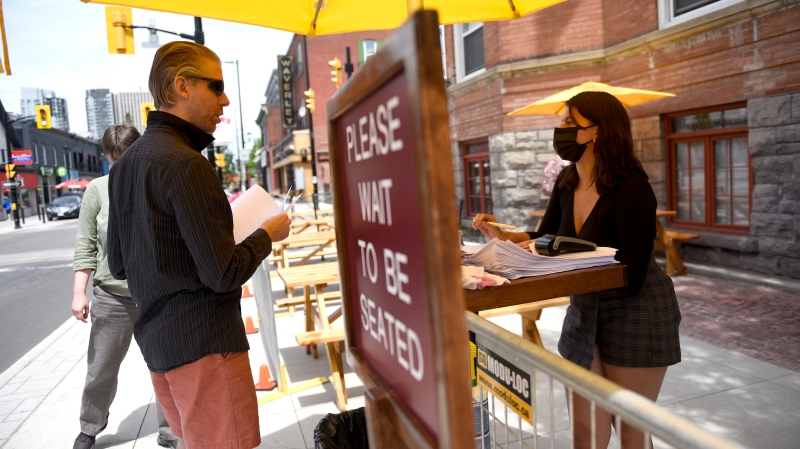 A server speaks to a patron as they arrive at an outdoor patio in Ottawa on the first day of Ontario's first phase of re-opening amidst the third wave of the COVID-19 pandemic, on Friday, June 11, 2021. THE CANADIAN PRESS/Justin Tang 