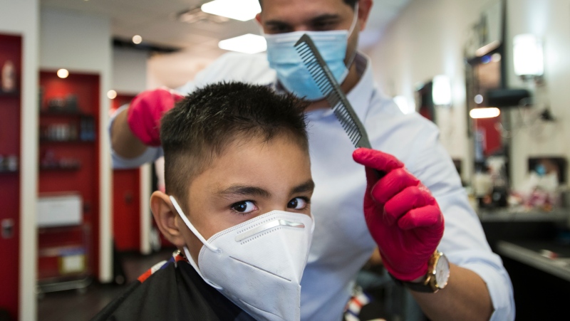 Five-year-old Aaren Tulsani gets his hair cut by owner and head barber Yasser Abbas, back, at Mohamad's Barber Shop during the COVID-19 pandemic in Cambridge, Ont., on Friday, June 12, 2020. THE CANADIAN PRESS/Nathan Denette 