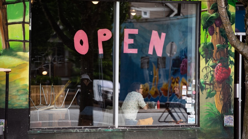A large "Open" sign is seen on a window as people sit inside a restaurant in Vancouver, on Sunday, May 31, 2020. THE CANADIAN PRESS/Darryl Dyck
