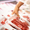 Closeup side view of unrecognizable woman chossing some fresh meat at local supermarket. The meat is cut into chops and packed into one pound packages. She has reached for a package of beef sirloin steaks.