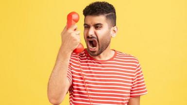 Angry nervous bearded man in striped t-shirt screaming and yelling talking retro landline phone, complaining on connection quality.