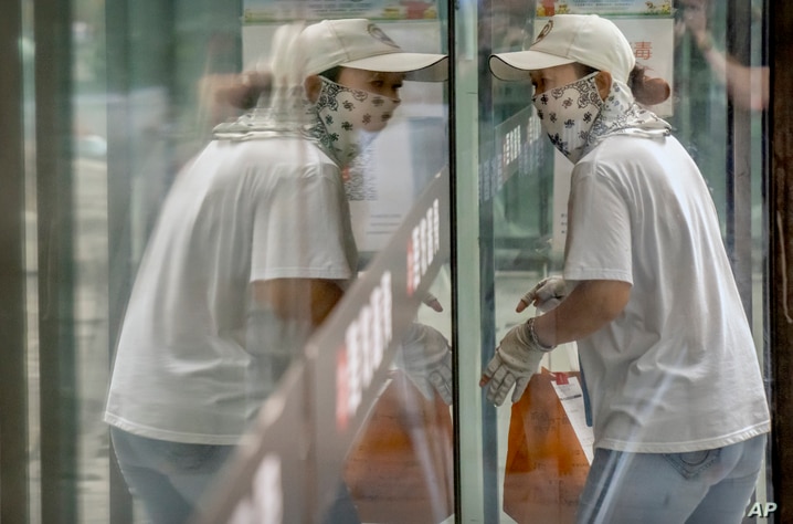 A delivery courier wearing a face mask to protect against COVID-19 is reflected in a window glass as she walks into a…
