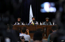 In front of a Taliban flag, Taliban spokesman Zabihullah Mujahid, center, speaks at his first news conference, in Kabul, Afghanistan, Aug. 17, 2021.