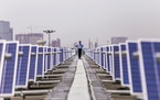 A security guard stands between solar panels implemented by Amplus Solar on the roof of the Yamaha Motor Co. plant in Surajpur, Uttar Pradesh, India, 