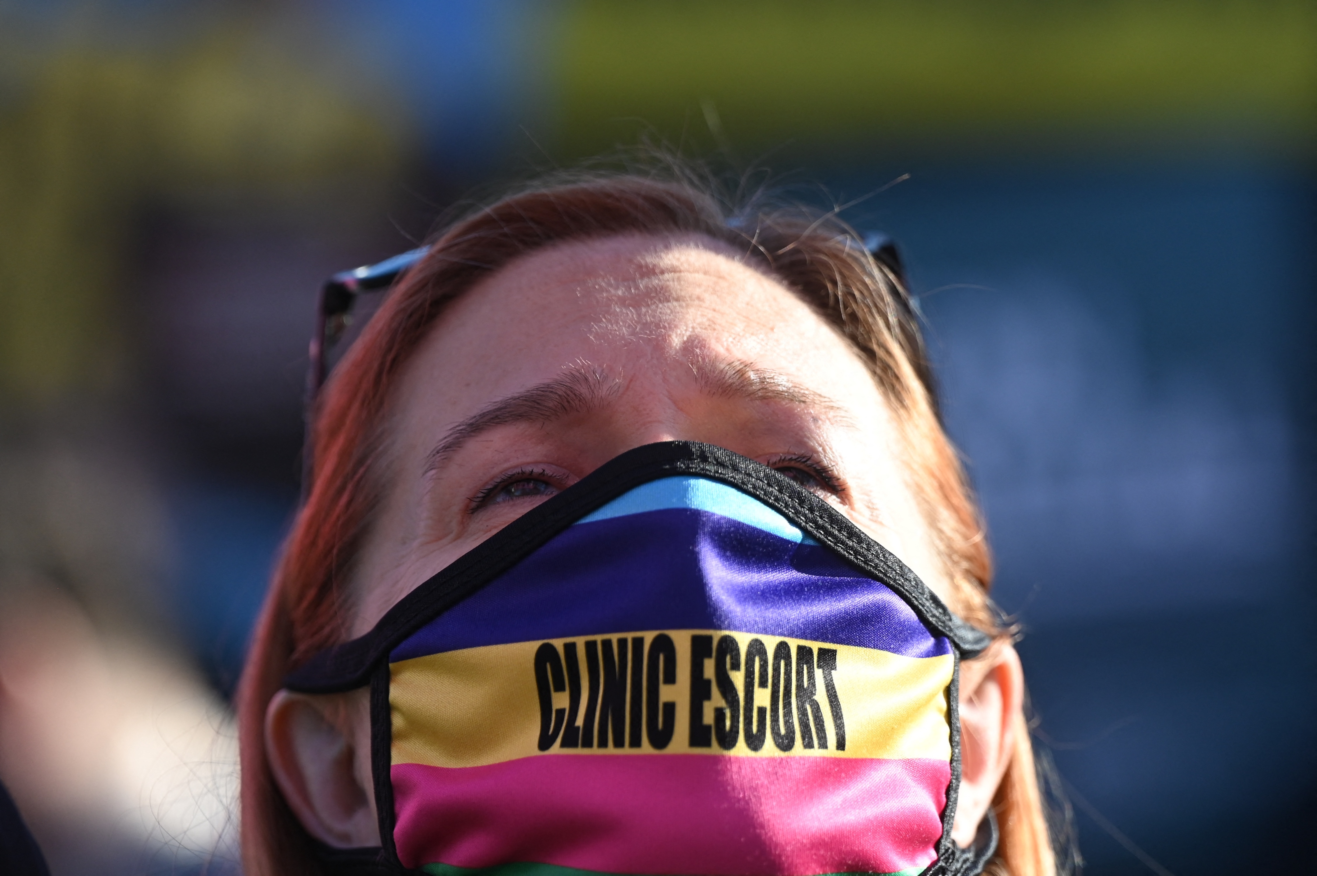 Face of a woman in a face mask that says Clinic Escort in bold black letters.
