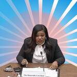 an illustration of Cori Bush, a brownskinned Black woman with long, black hair, sitting at a desk and surrounded by light blue rays