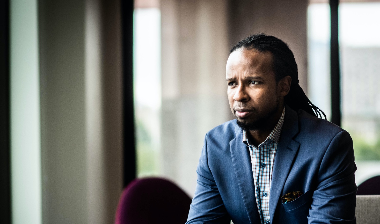 Photo of Ibram X. Kendi sitting in a blue suit looking out a window.