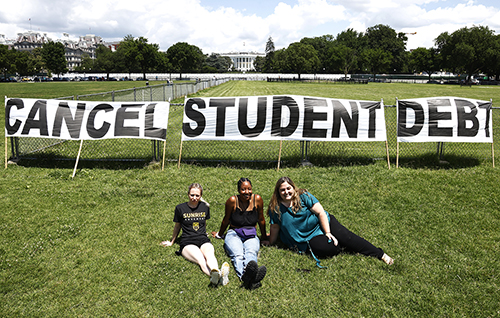 Photo of three supporters of student loan debt cancellation displaying a banner near the White House on June 15, 2021.