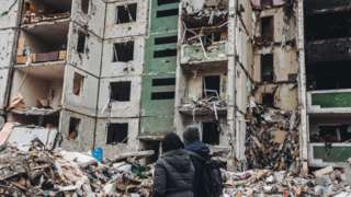 People look at a destroyed building in Chernihiv