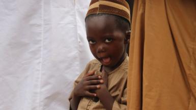 A young boy makes a funny face at the camera during prayers.