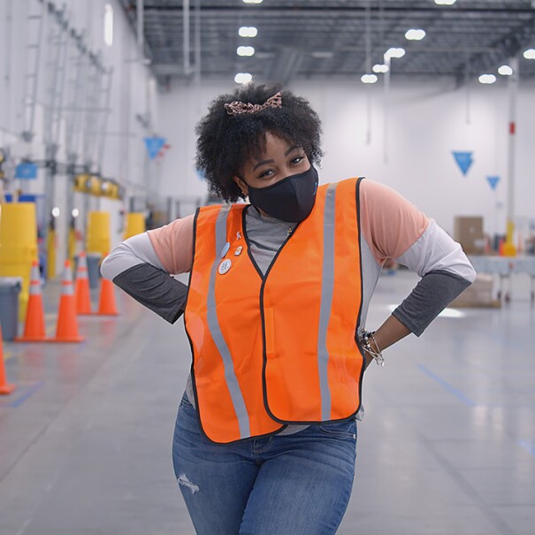 a Black woman who is an Amazon employee looks at the camera. She is wearing a face mask.