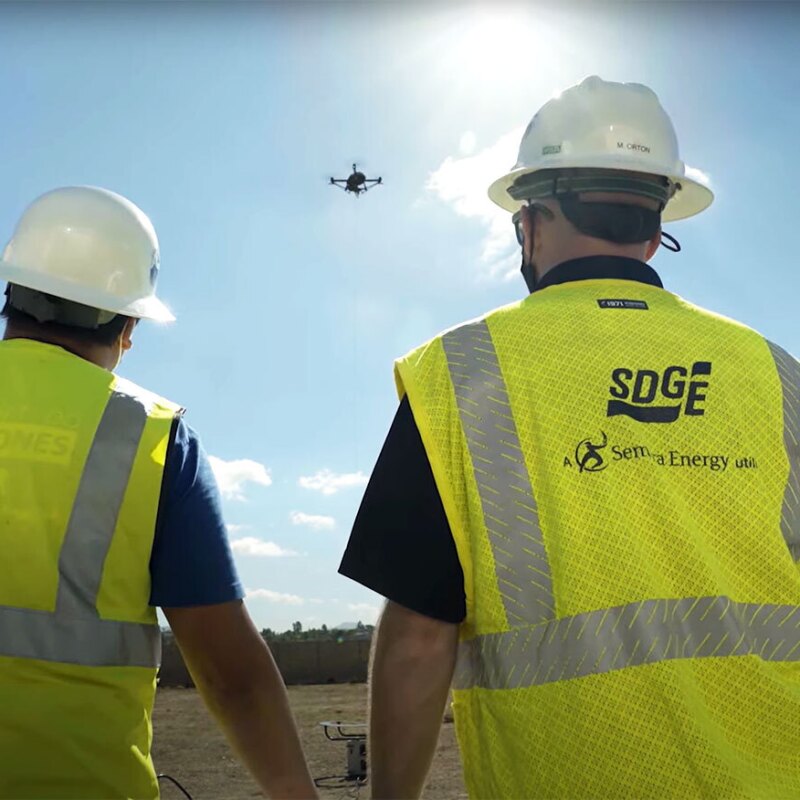 An image of two men looking up at the sky at a drone in the air.