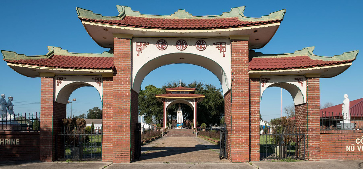 A front view of the Queen of Peace Shrine and Gardens in a largely Vietnamese neighborhood of Port Arthur, Texas. A large, three-part arch framing a garden with statuary inside
