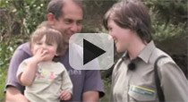 Link to video, showing a young woman in a Department of Conservation uniform, standing with a man holding a toddler. 