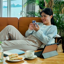 Smiling pretty young woman, relaxes on the sofa in her living room while using her mobile smart phon...