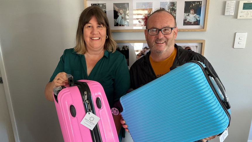 Man and woman holding up a blue and pink suitcase.