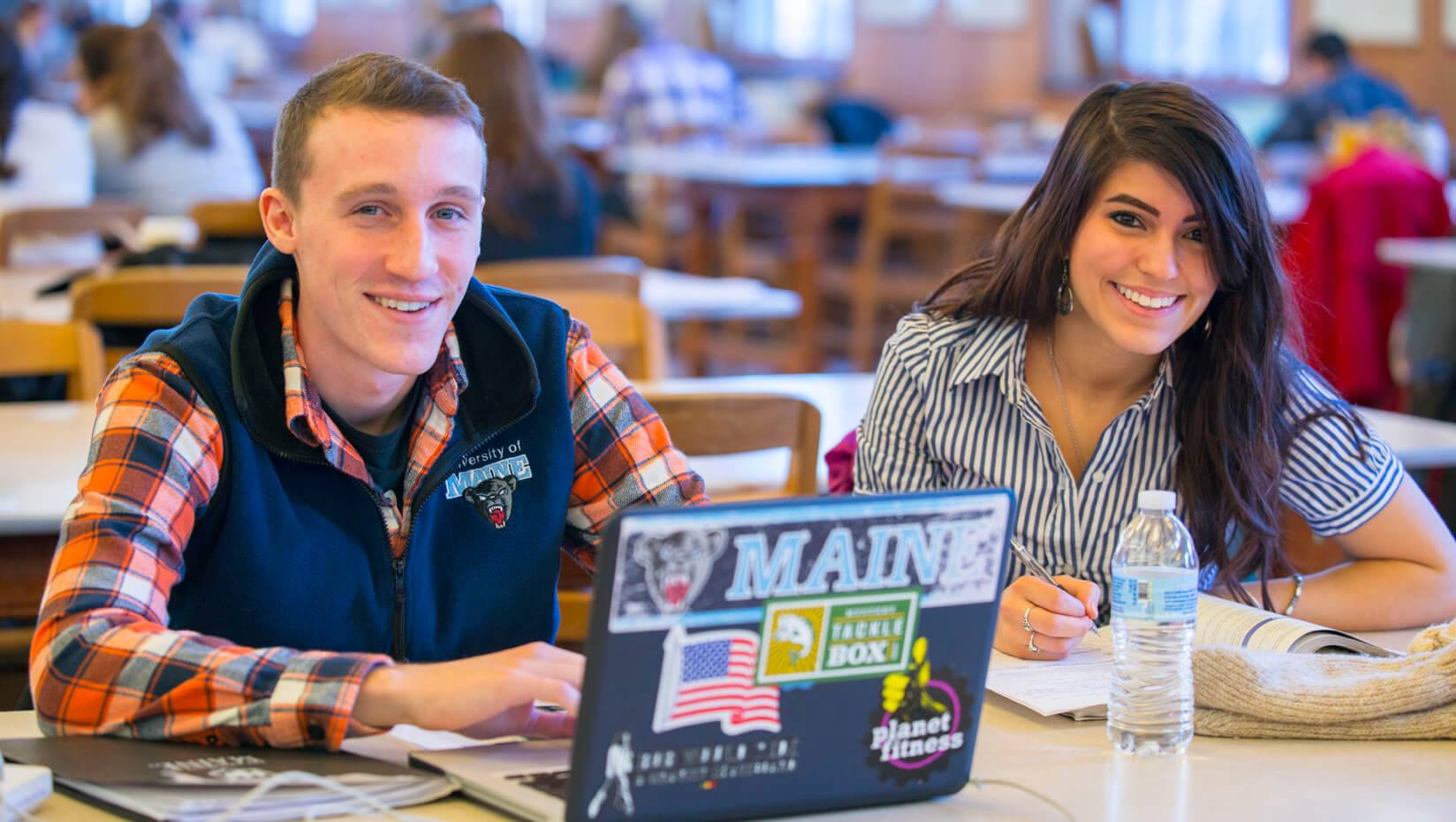 UMaine students in Fogler Library smiling with laptop