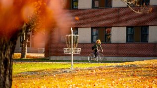 Student riding a bike on campus with autumn colors