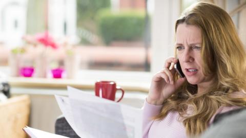 Woman frustratedly calls company on the phone while holding a bill
