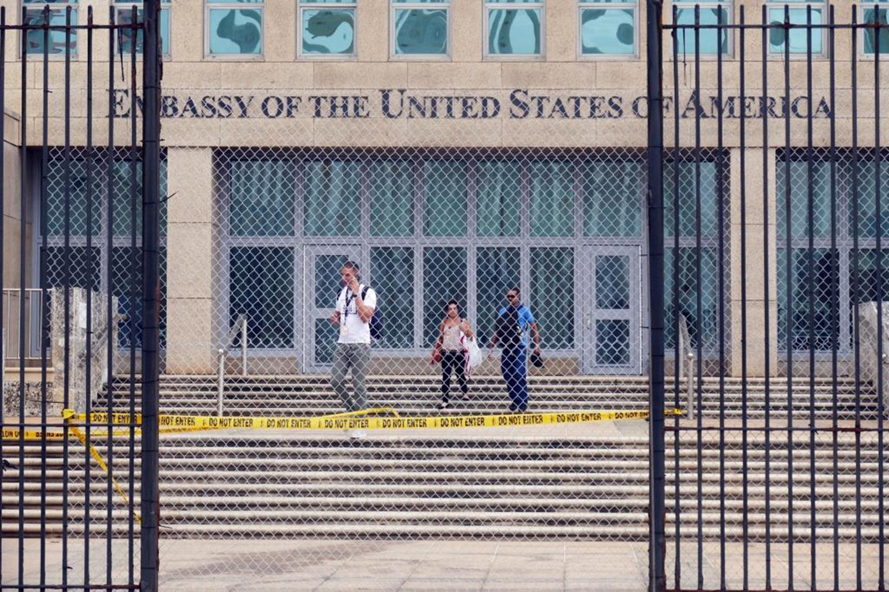 People on the steps of a building titled Embassy of the United States of America, seen through an open wrought iron gate.