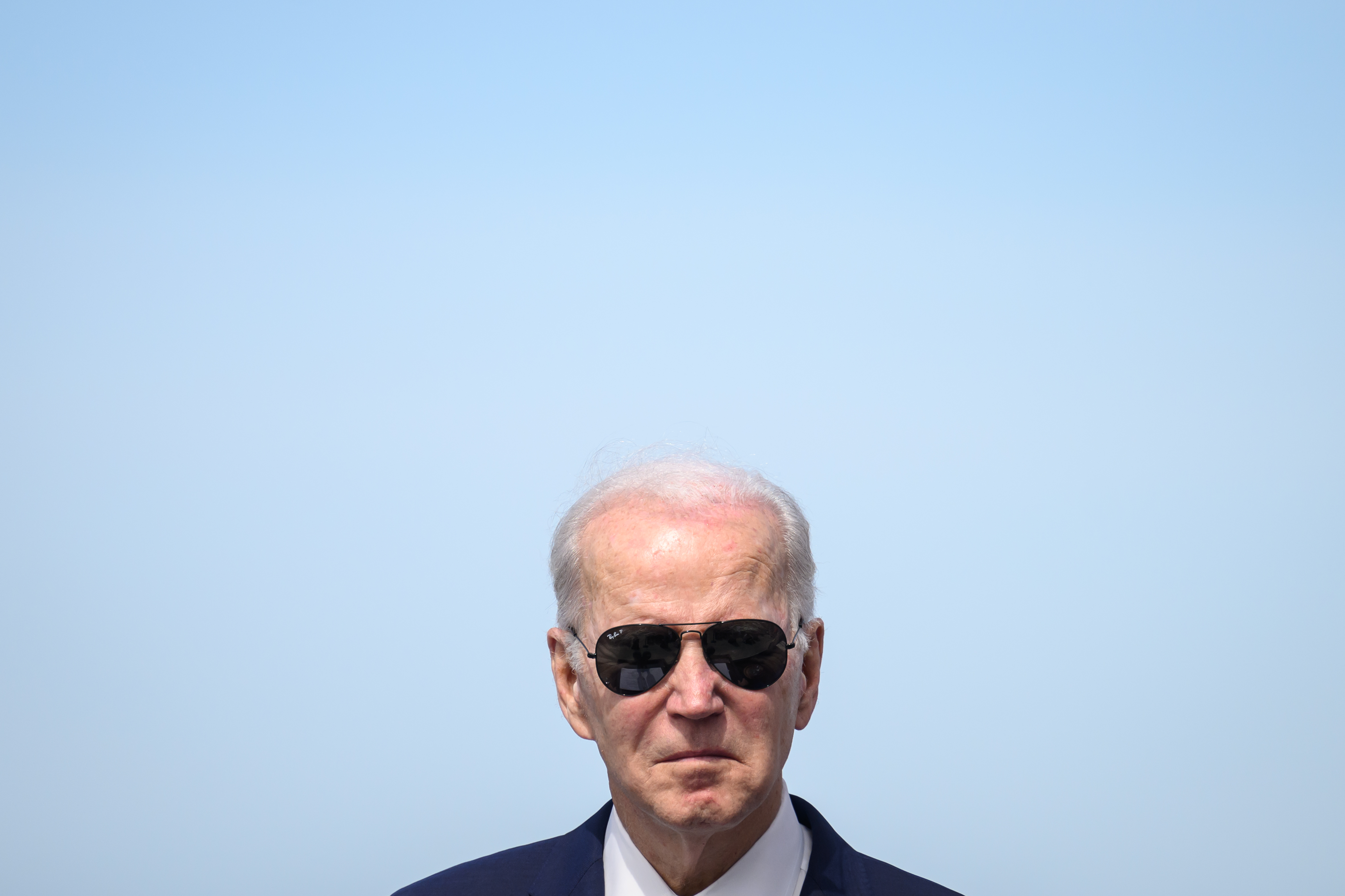 A photo of President Joe Biden wearing sunglasses, against a blue sky.