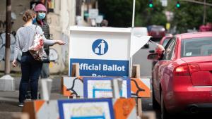 Photo of a ballot drop site with voters dropping off their ballot.
