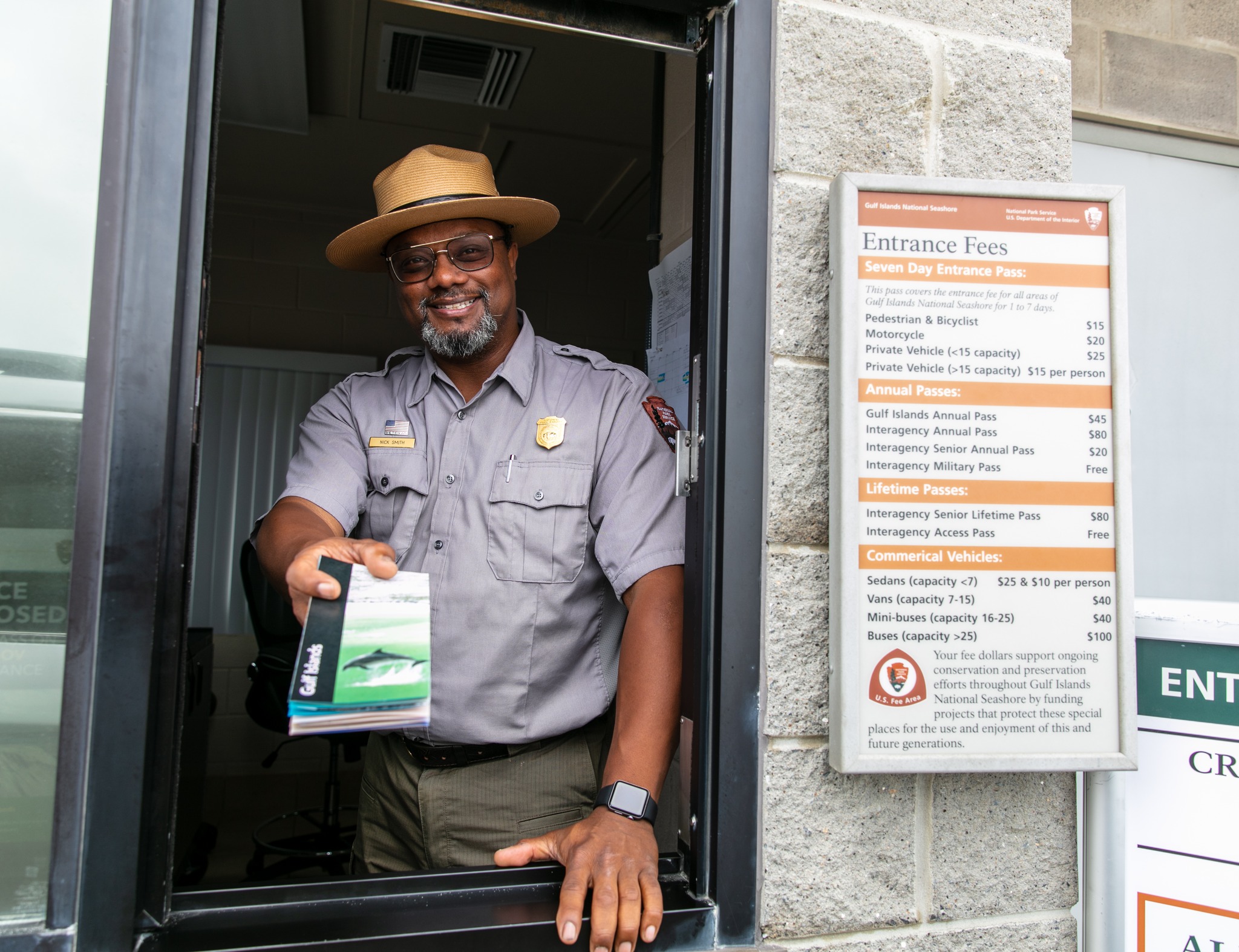 A smiling park ranger hands a brochure through the window of an entrance station.  