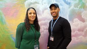A smiling Black man and woman stand in front of a dreamy mural