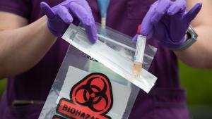 close up of a health worker in purple scrubs dropping a specimen vial into a red biohazard bag