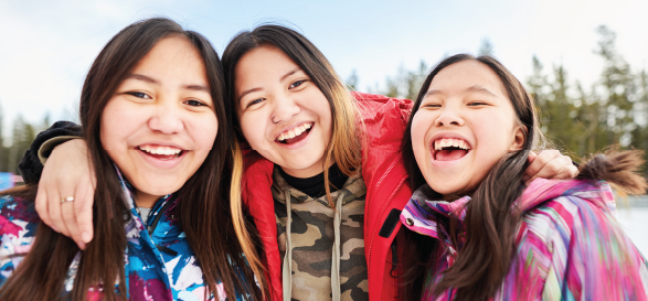 three girls in winter jackets hugging and smiling in the snow