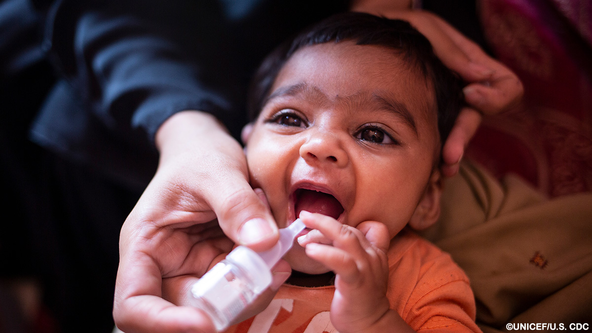 An adult holds a dropper containing oral polio vaccine near the open mouth of an infant.